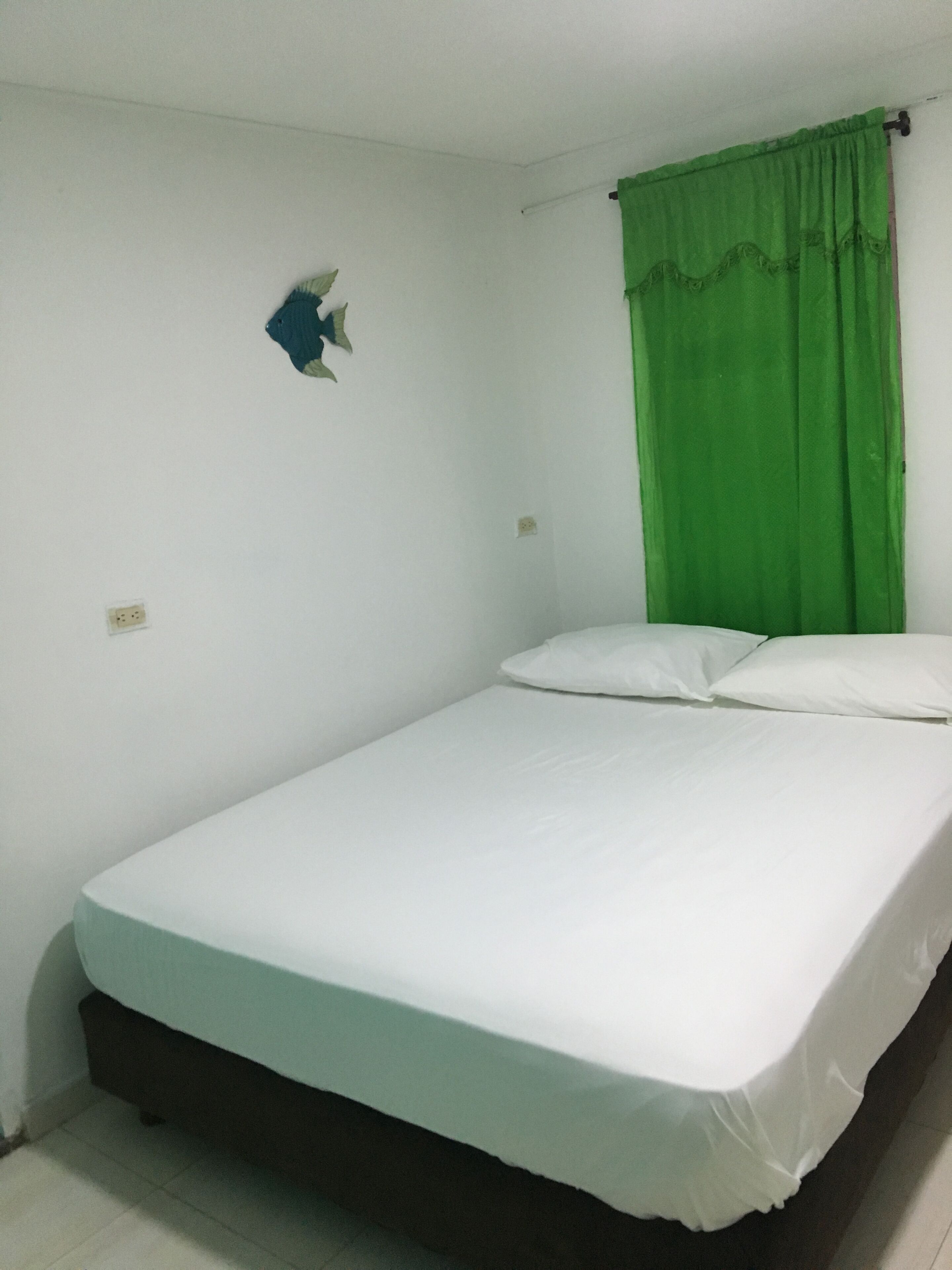 A single bed with white bedding in a room with white walls, a green curtain, and a small decorative item on the wall.
