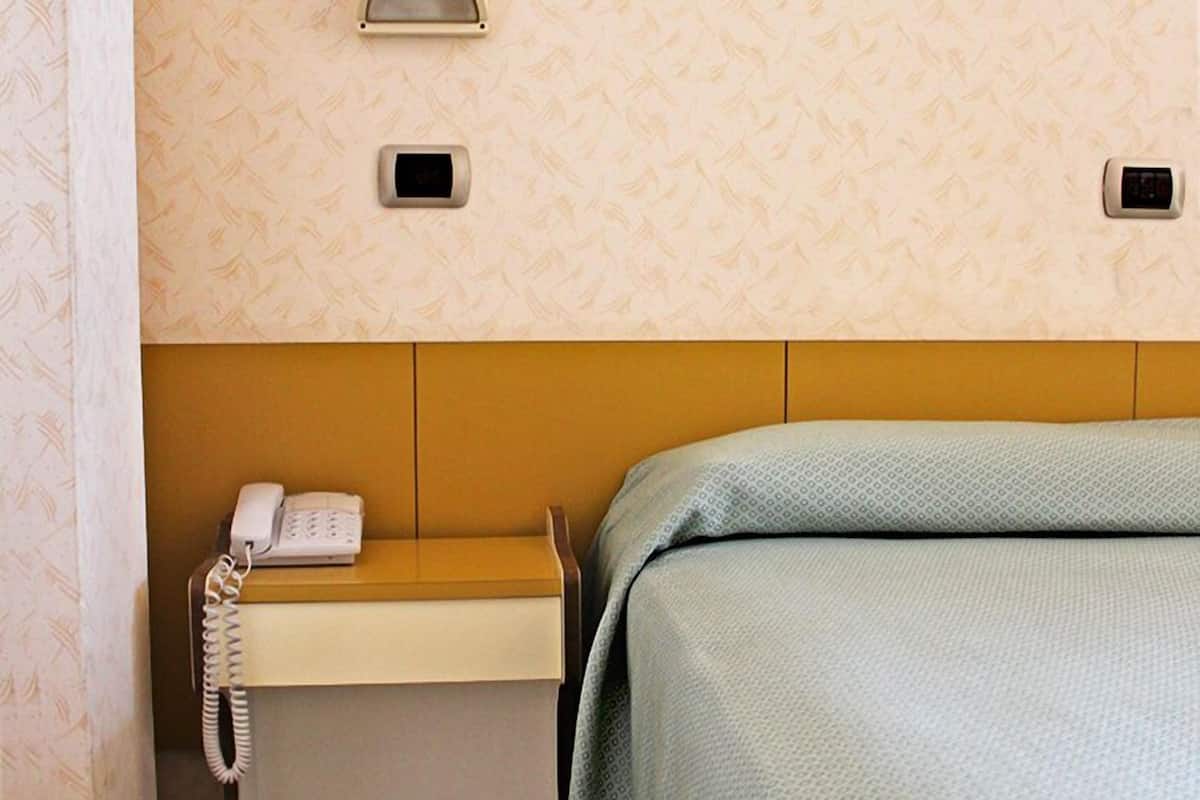 A hotel room with a bed, a bedside table with a phone, and a wall-mounted light fixture.