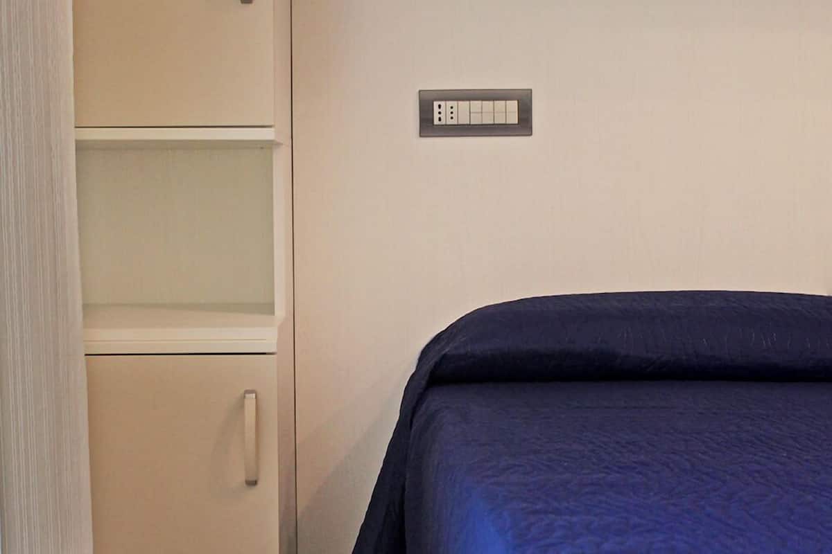 A room with a bed, a wardrobe, and a wall-mounted electrical outlet.