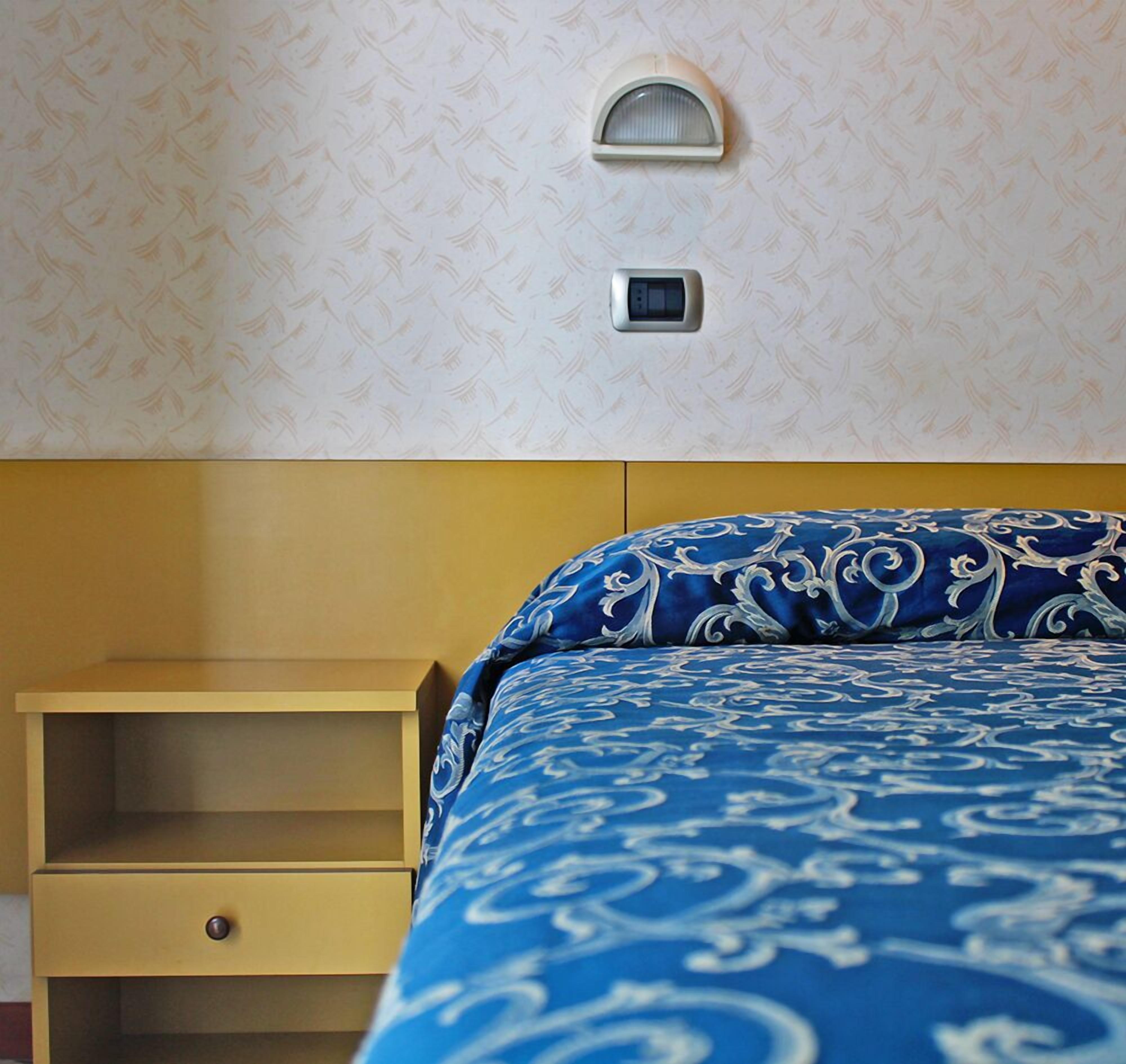 A hotel room with a bed, a bedside table, and a wall-mounted light fixture.