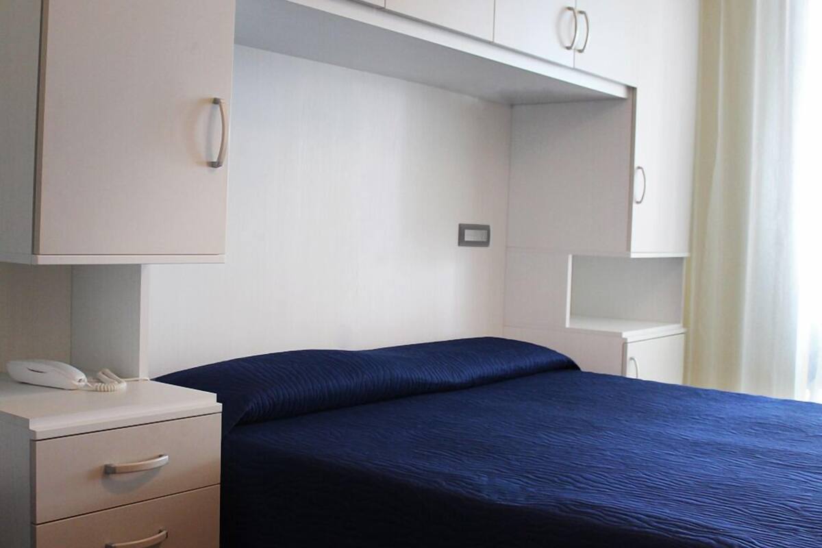 A bedroom with a bed, a bedside table with a phone, and a wardrobe with two doors.