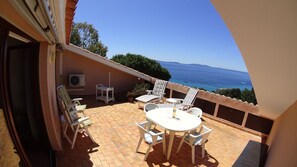 A balcony with a table and chairs, overlooking the sea.