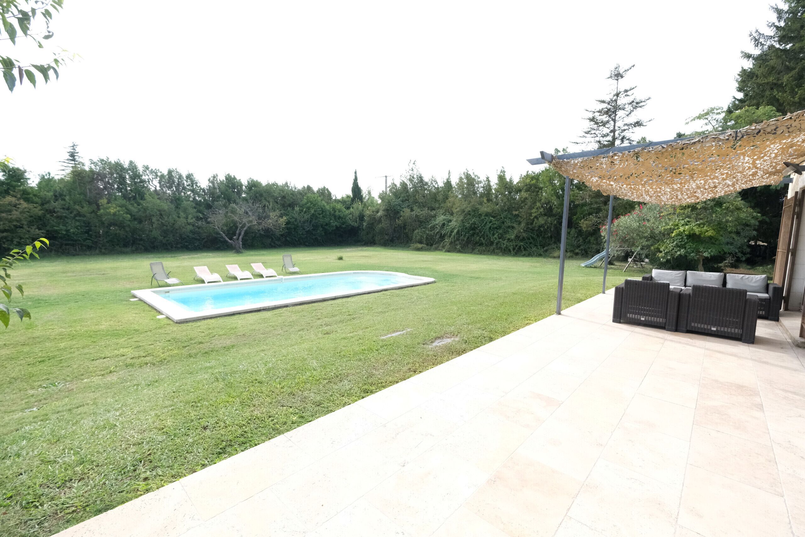 Un jardin avec une piscine, des chaises longues et du mobilier d’extérieur.