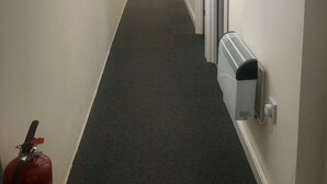 A narrow hallway with a carpeted floor, white walls, and a fire extinguisher on the left. - Eazzzy rooms Corby (Corby)
