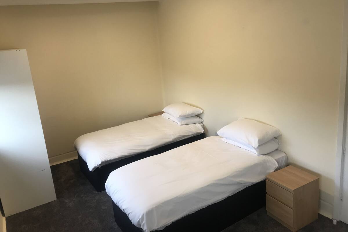 A small, clean room with two single beds, a wooden nightstand, and a white wardrobe.