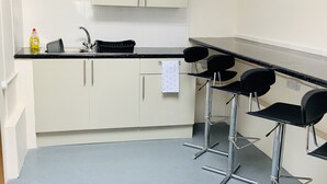 A kitchenette with a sink, cabinets, and a countertop. There are three bar stools and a black chair. - Eazzzy rooms Corby (Corby)