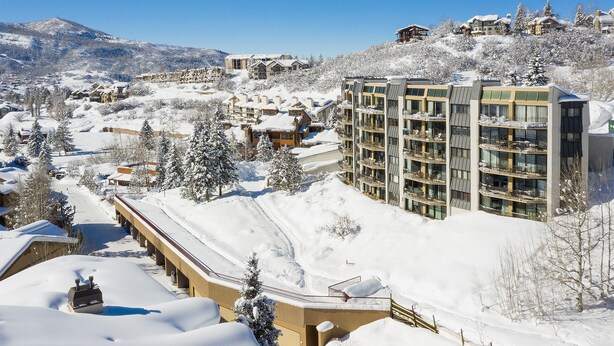 Een bergresort bedekt met sneeuw, met meerlaags gebouwen, waaronder een hotel met balkons en een skilift.