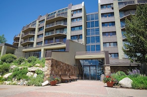 Un hotel de varios pisos con balcones, fachada de piedra y entrada ajardinada.