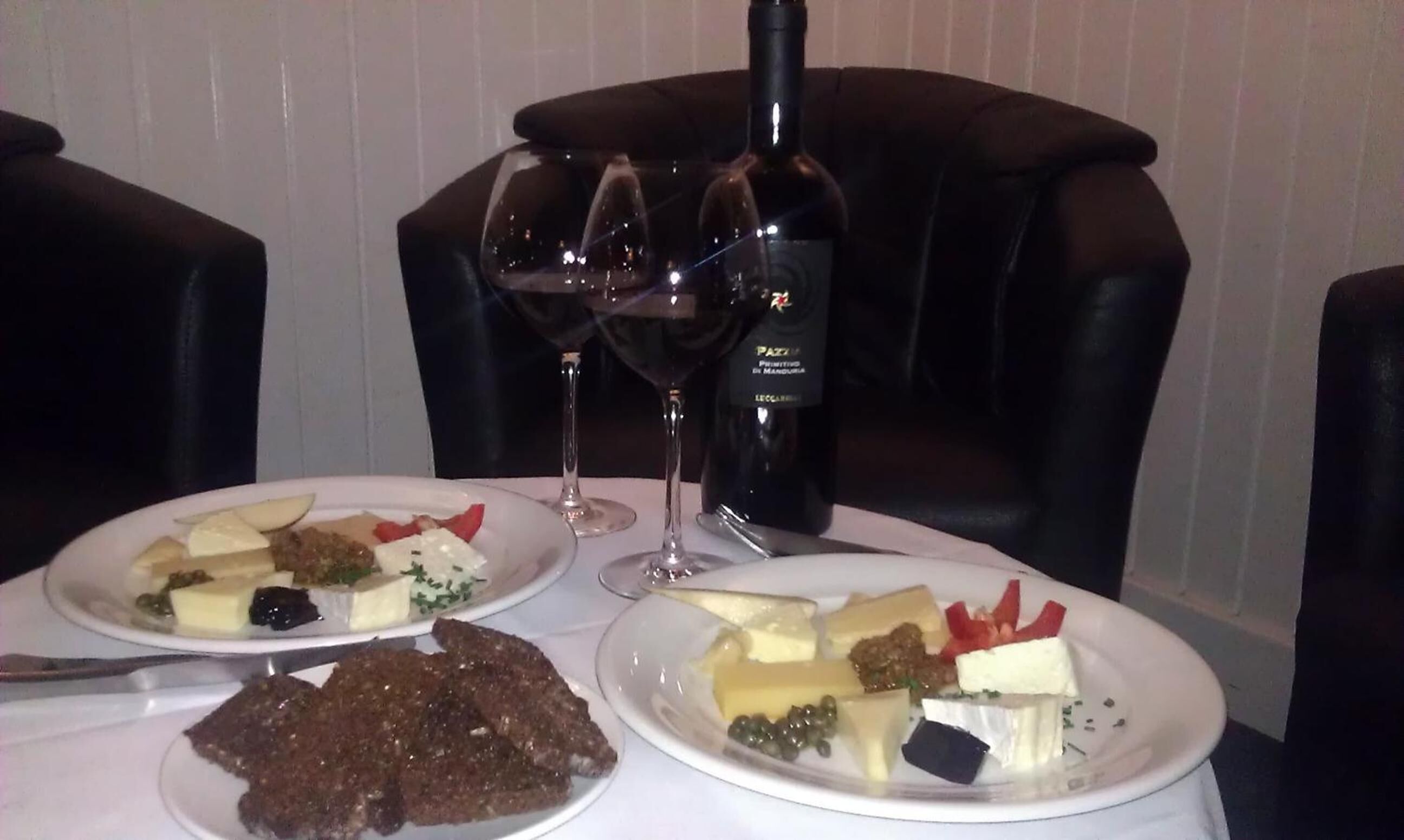 Een tafel met twee kaasplaten, een fles wijn en twee wijnglazen.