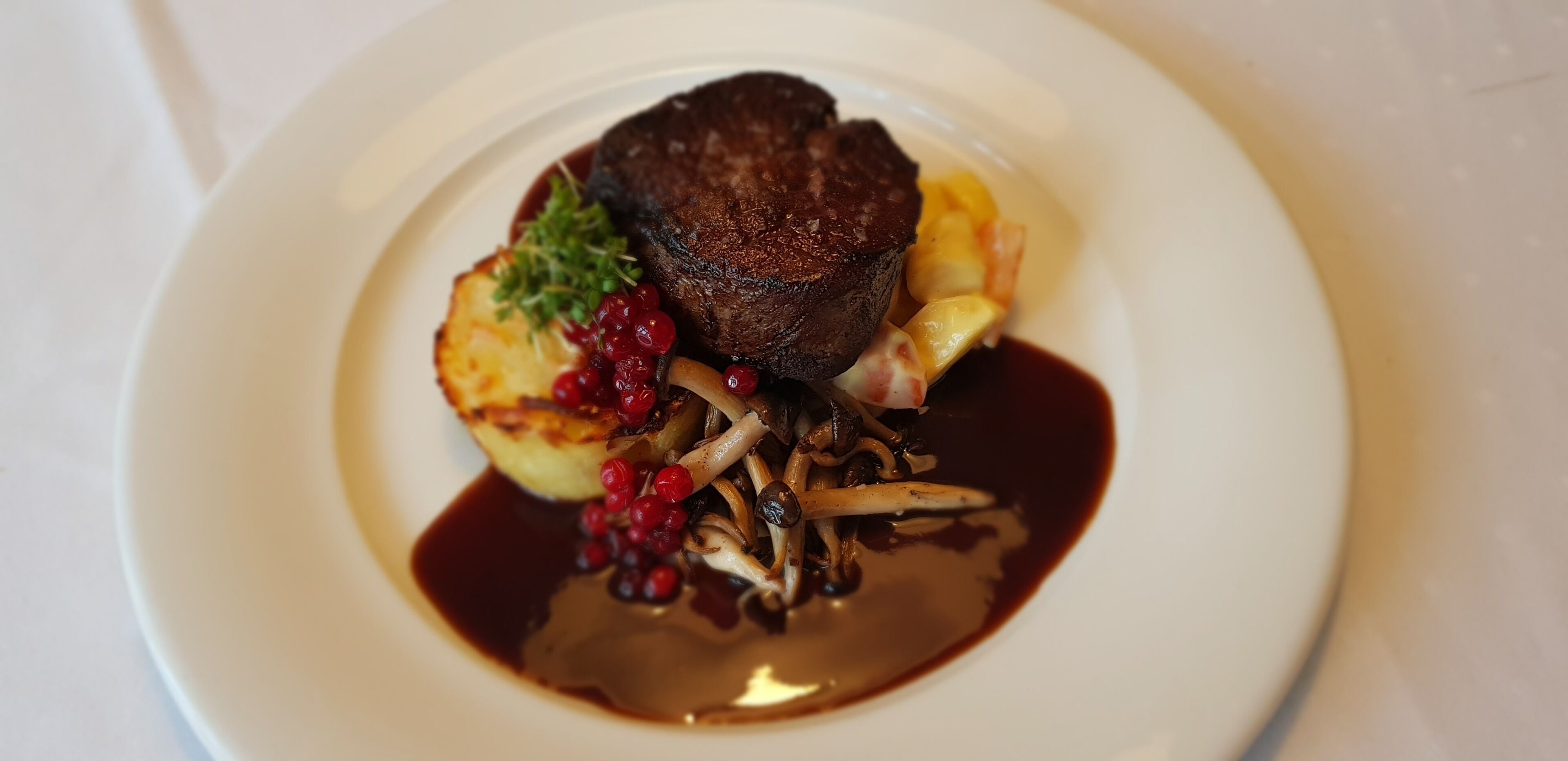 A plate of food with a piece of meat, potatoes, and red berries.
