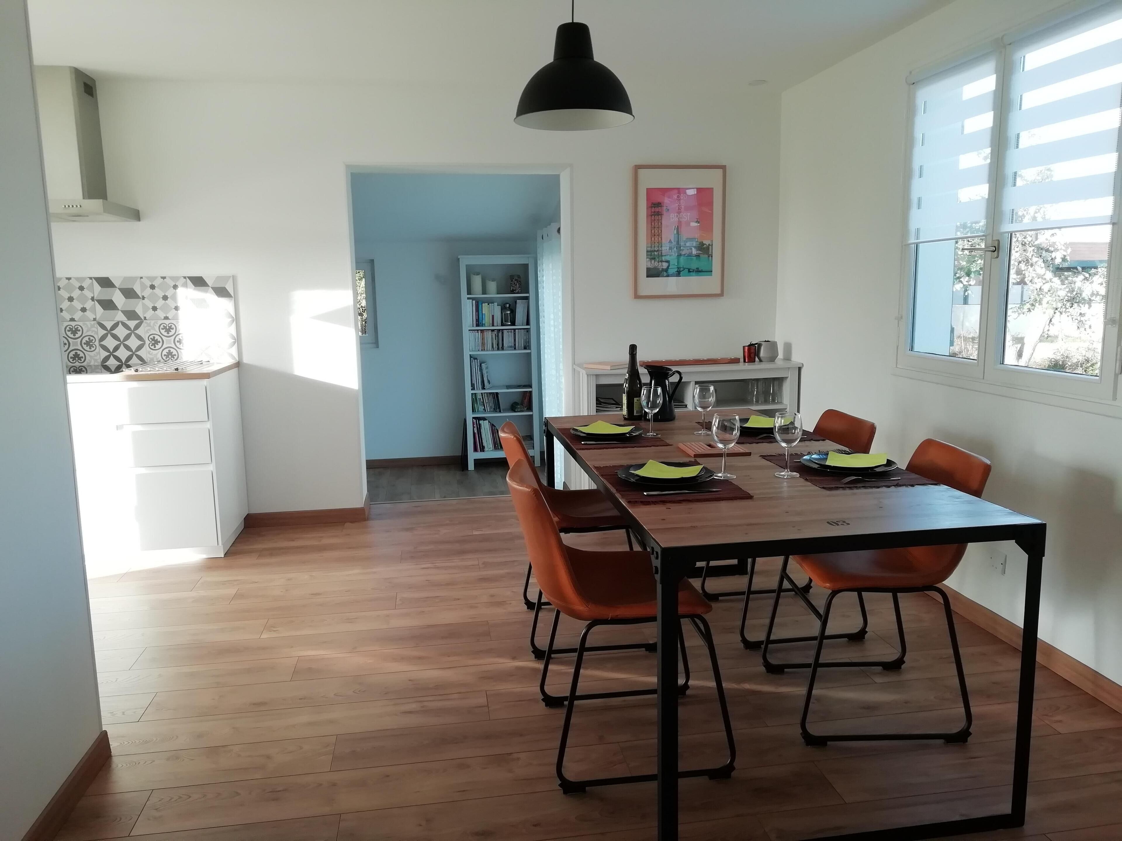 A dining area with a wooden table, orange chairs, and a black pendant light.