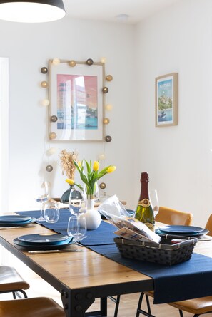 A dining table set with plates, glasses, and a bottle, surrounded by chairs and a vase with flowers.