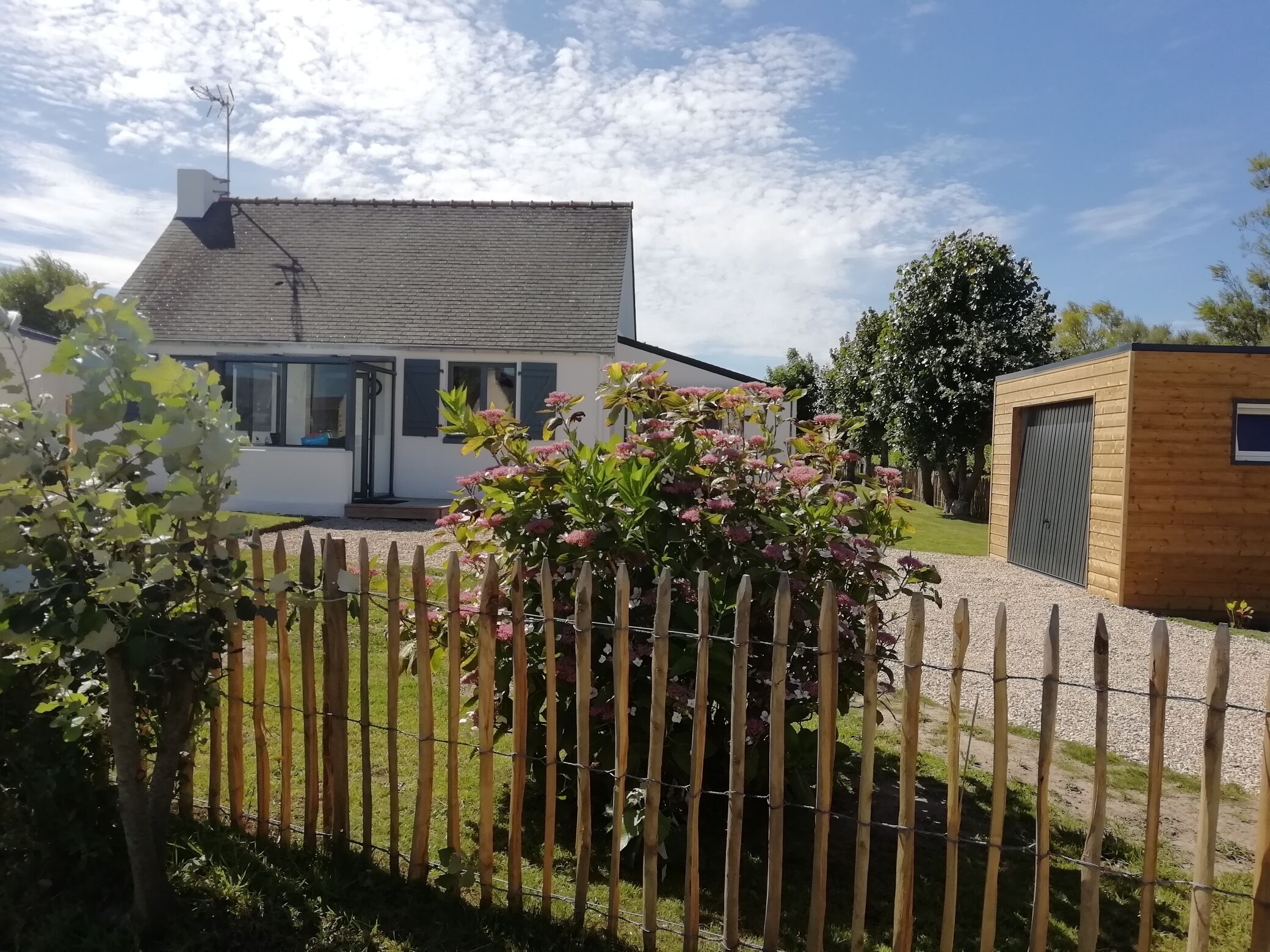Ein Haus mit schrägem Dach, Holzzaun und Garten mit rosa Blüten.
