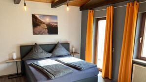 Een moderne slaapkamer met een groot bed, twee nachtkastjes, een aan de muur hangend schilderij en oranje gordijnen.