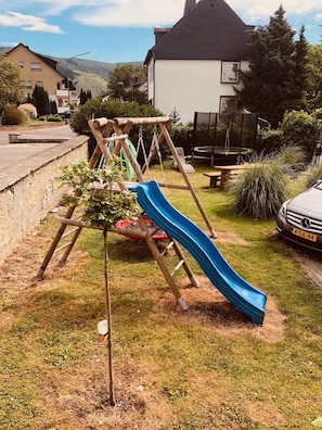 Une aire de jeux avec un toboggan et des balançoires, située dans un quartier résidentiel.