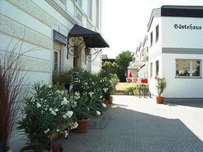 En bygning med skilt, der siger 'Gästehaus', og en belagt gårdsplads med plantekasser og udendørs siddepladser.