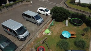Een parkeerplaats met meerdere auto's, een speeltuin met een glijbaan en schommel, en een trampoline.