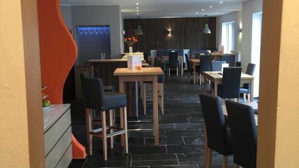 Een moderne eetruimte met zwart betegelde vloer, houten tafels en zwarte stoelen.