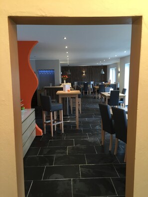 A modern dining area with black tiled flooring, wooden tables, and black chairs.