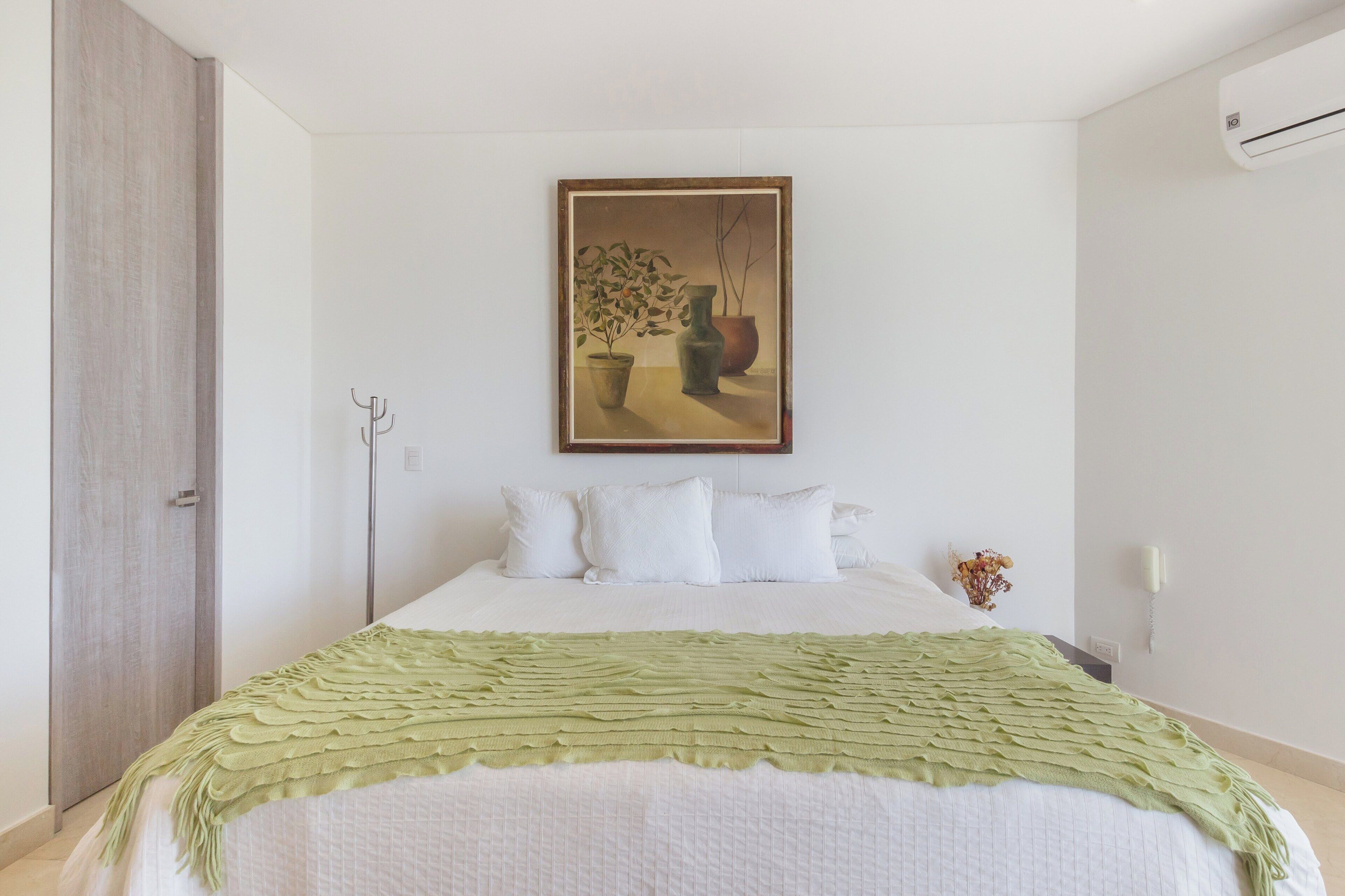 A bedroom with a bed, a green blanket, a painting on the wall, and a wooden wardrobe.