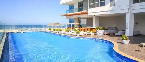 Un hotel moderno con una gran piscina, zona de estar exterior y vistas al océano.