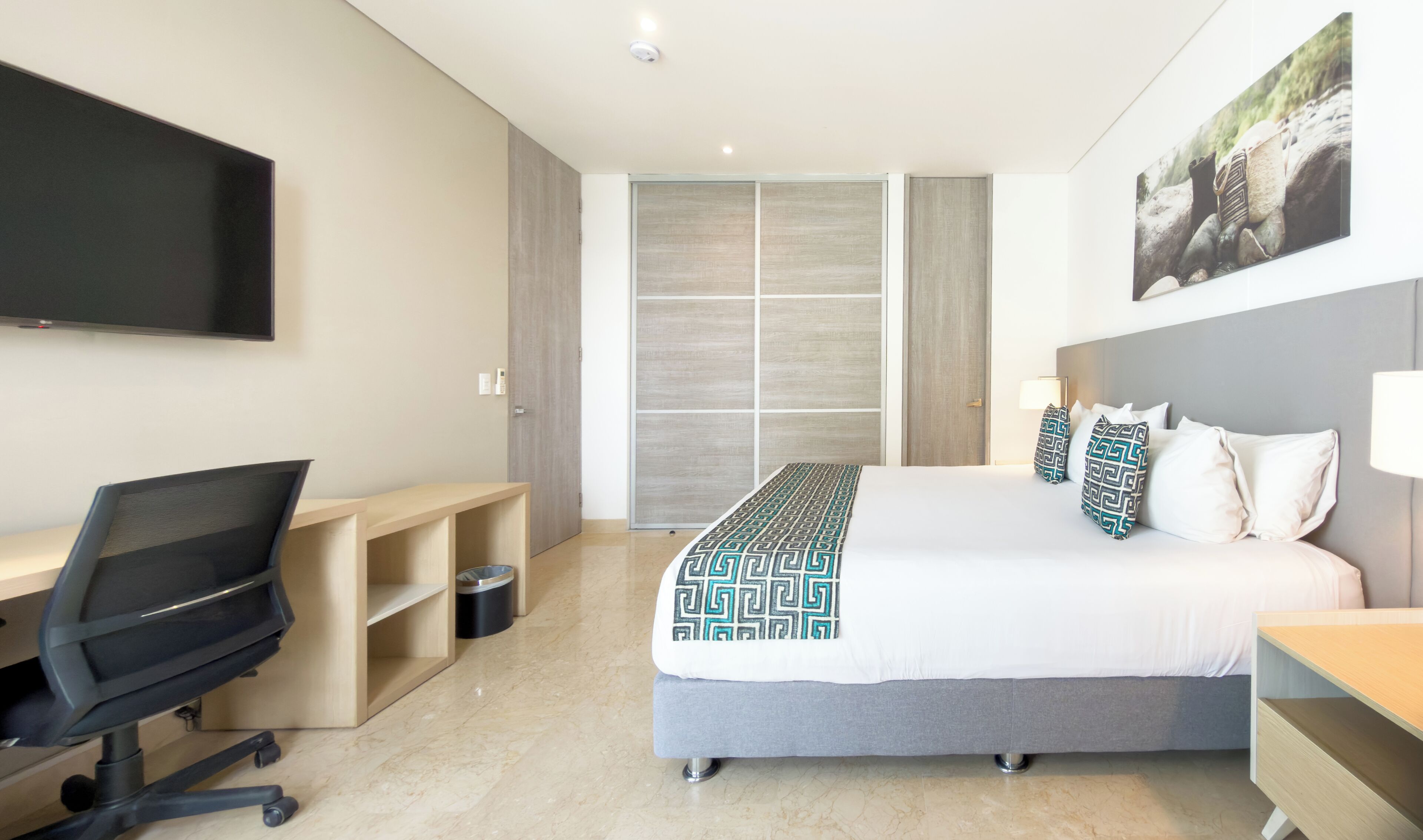 A hotel room with a bed, a desk, a chair, a television, and a wardrobe.