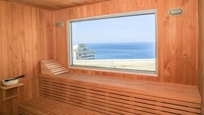 A wooden sauna with a large window offering a view of the beach and ocean. - Grand Marina Santa Marta (Santa Marta)