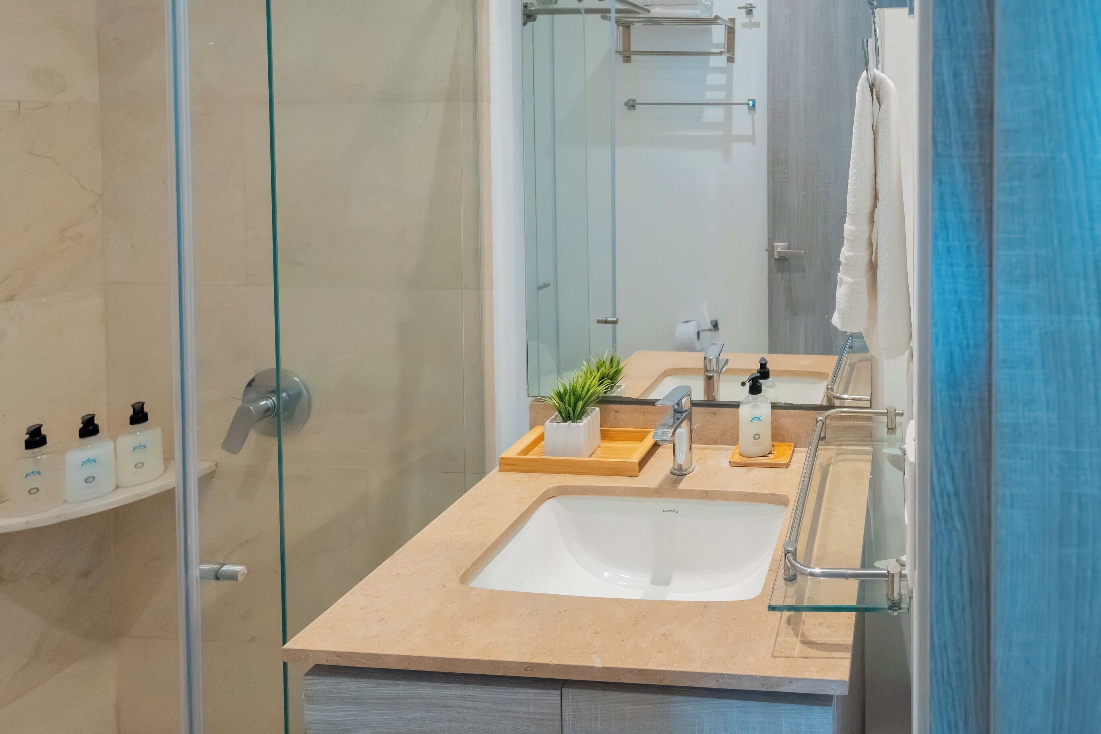 A modern bathroom with a glass shower enclosure, a beige countertop, a white sink, and a mirror.
