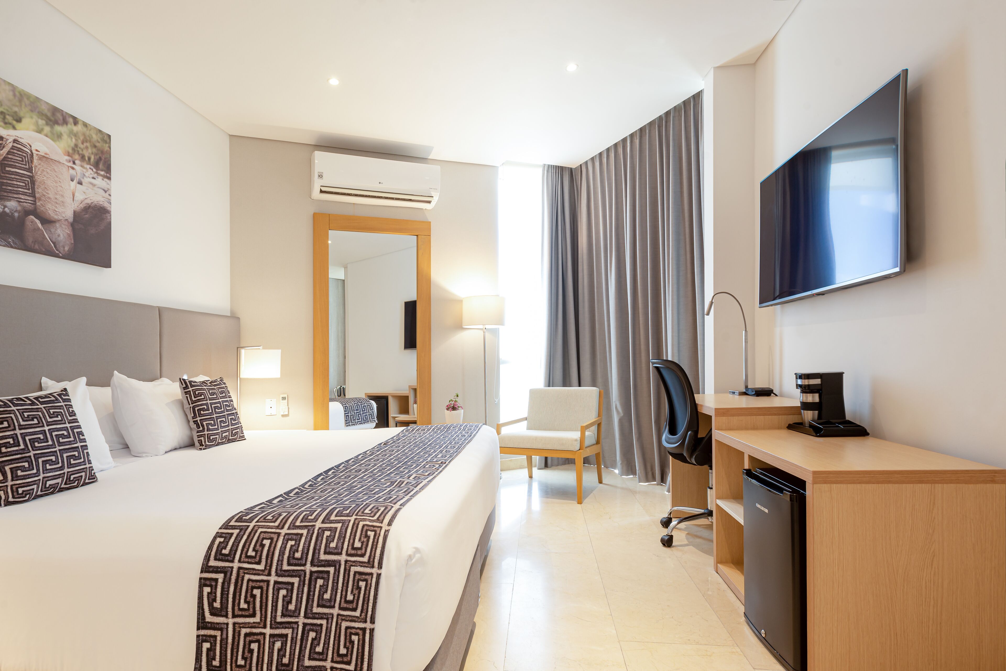 Ein modernes Hotelzimmer mit einem großen Bett, einem Schreibtisch mit Kaffeemaschine, einem Fernseher und einem Sessel.