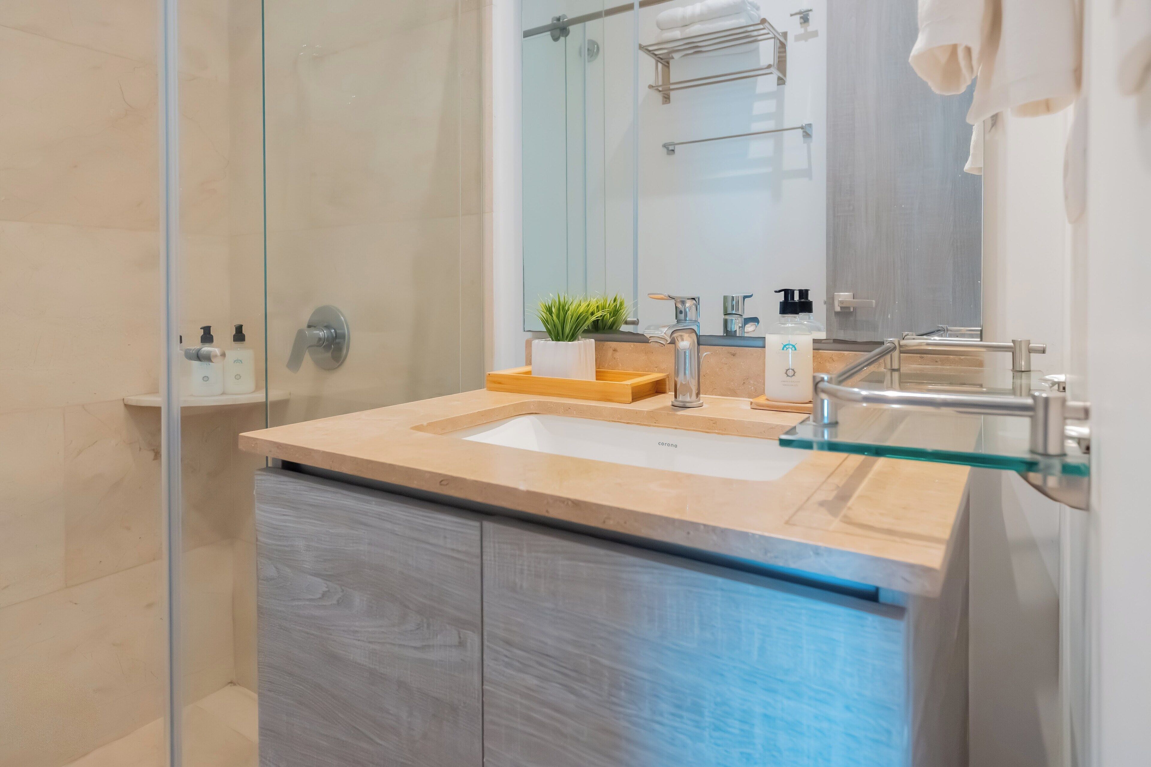 A modern bathroom with a glass shower enclosure, a beige countertop, and a large mirror.