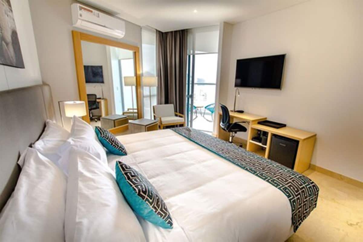 A hotel room with a bed, desk, chair, TV, and a large mirror.