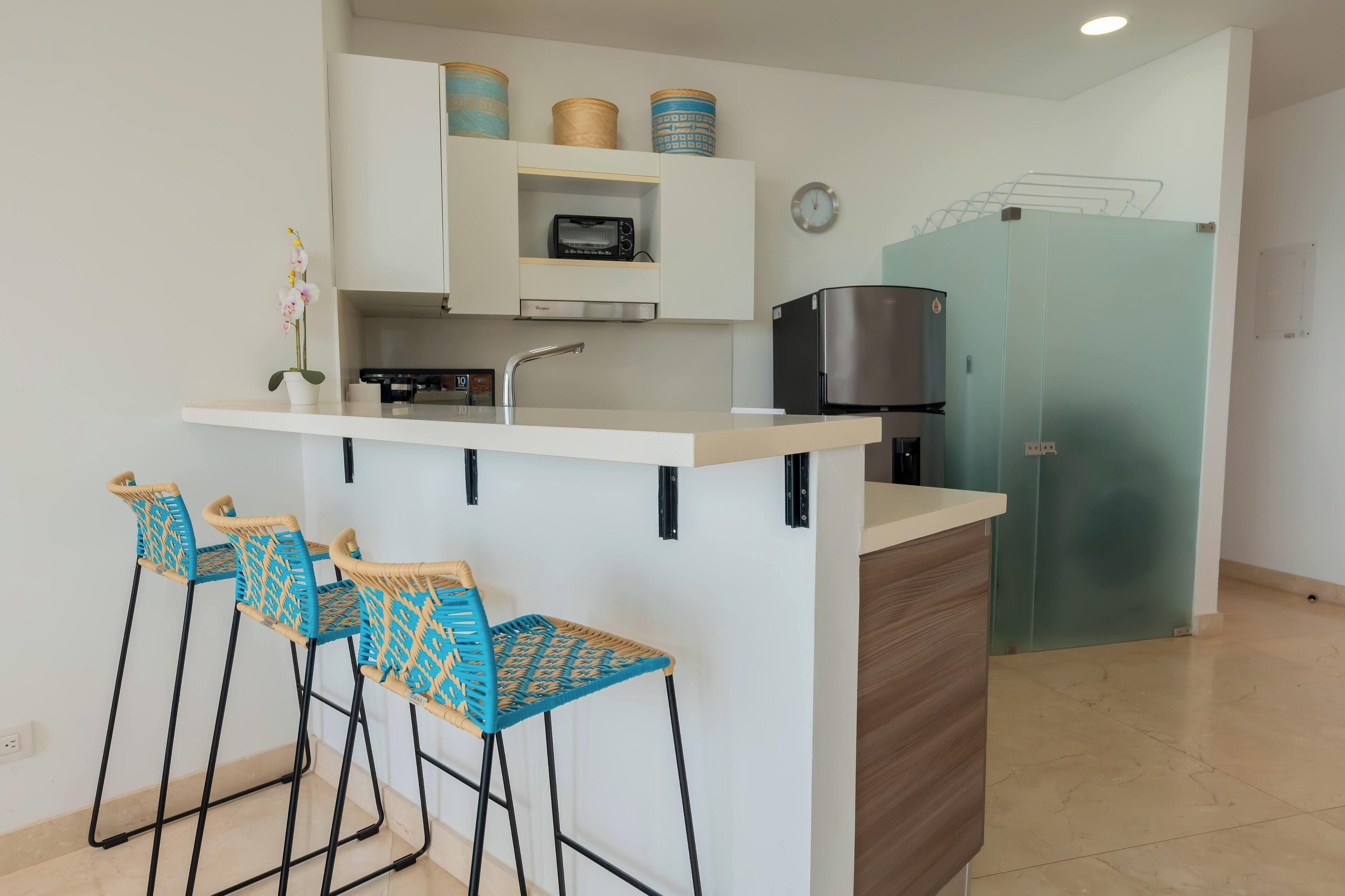 A compact kitchen with a central island, bar stools, a microwave, a toaster, and a refrigerator.