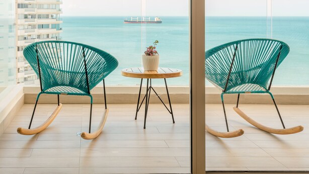 A balcony with two rocking chairs and a small table, overlooking a clear sea and a distant pier. - Grand Marina Santa Marta (Santa Marta)