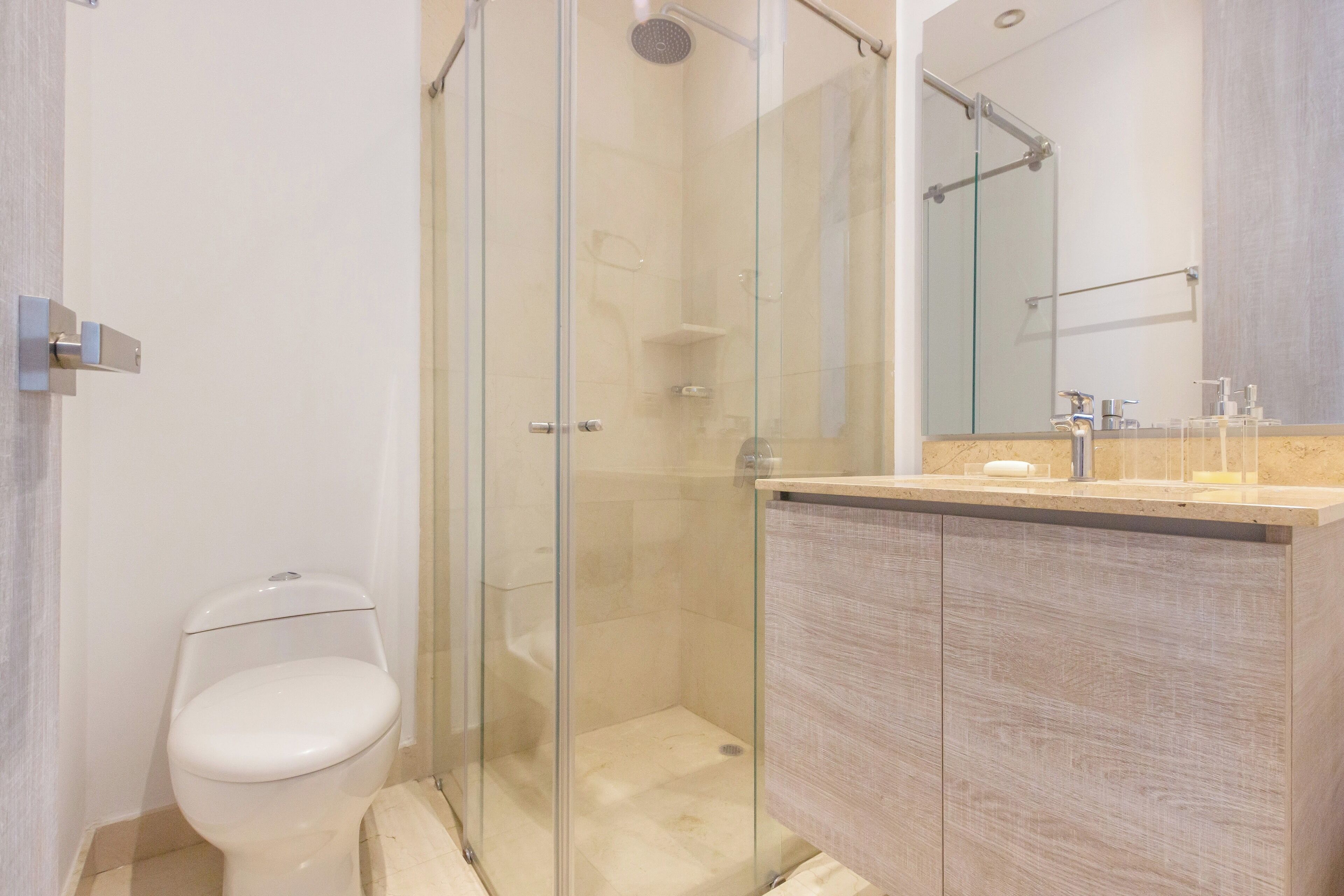 A modern bathroom with a glass-enclosed shower, a toilet, and a vanity with a mirror.