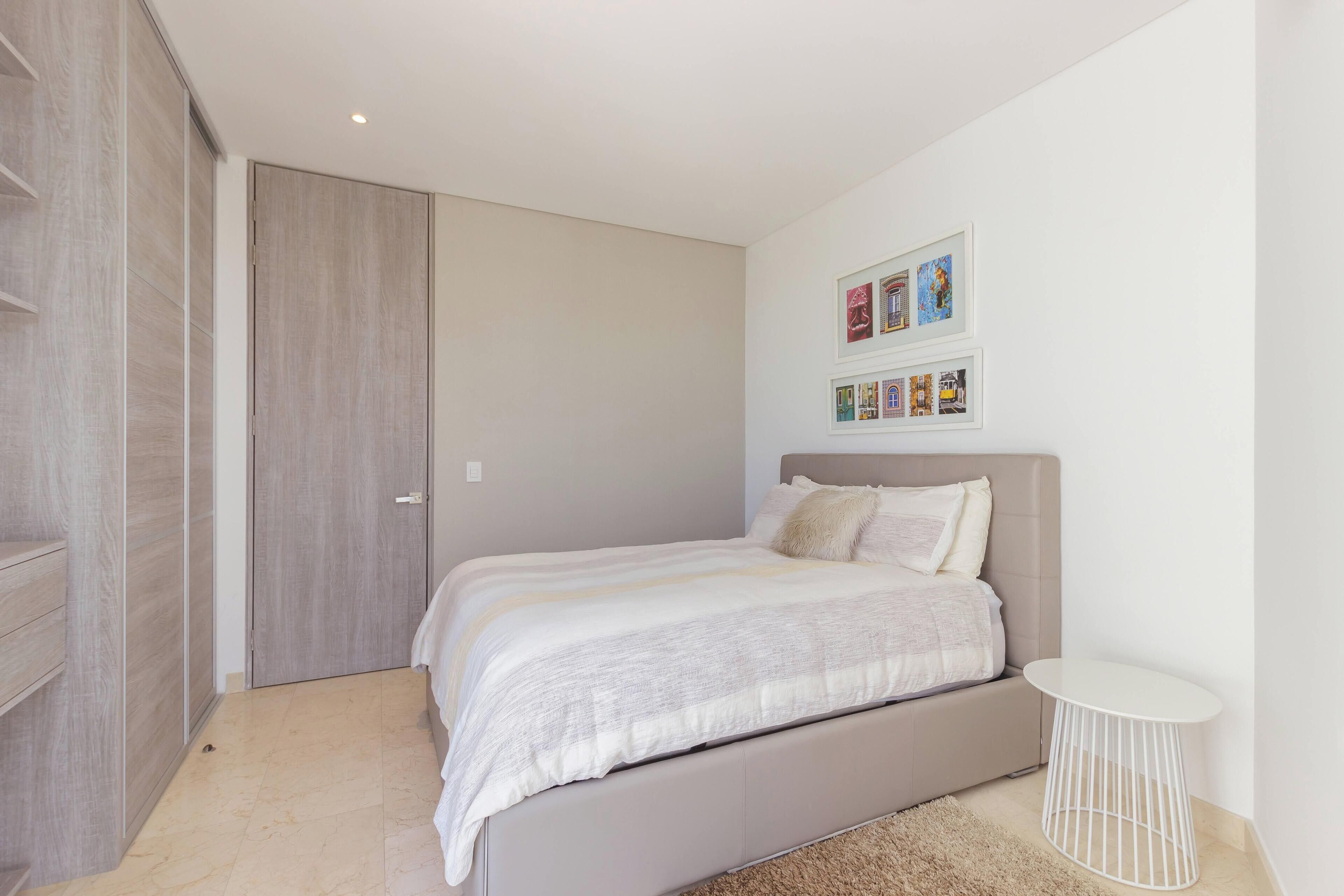 A bedroom with a bed, a bedside table, a wardrobe, and framed pictures on the wall.