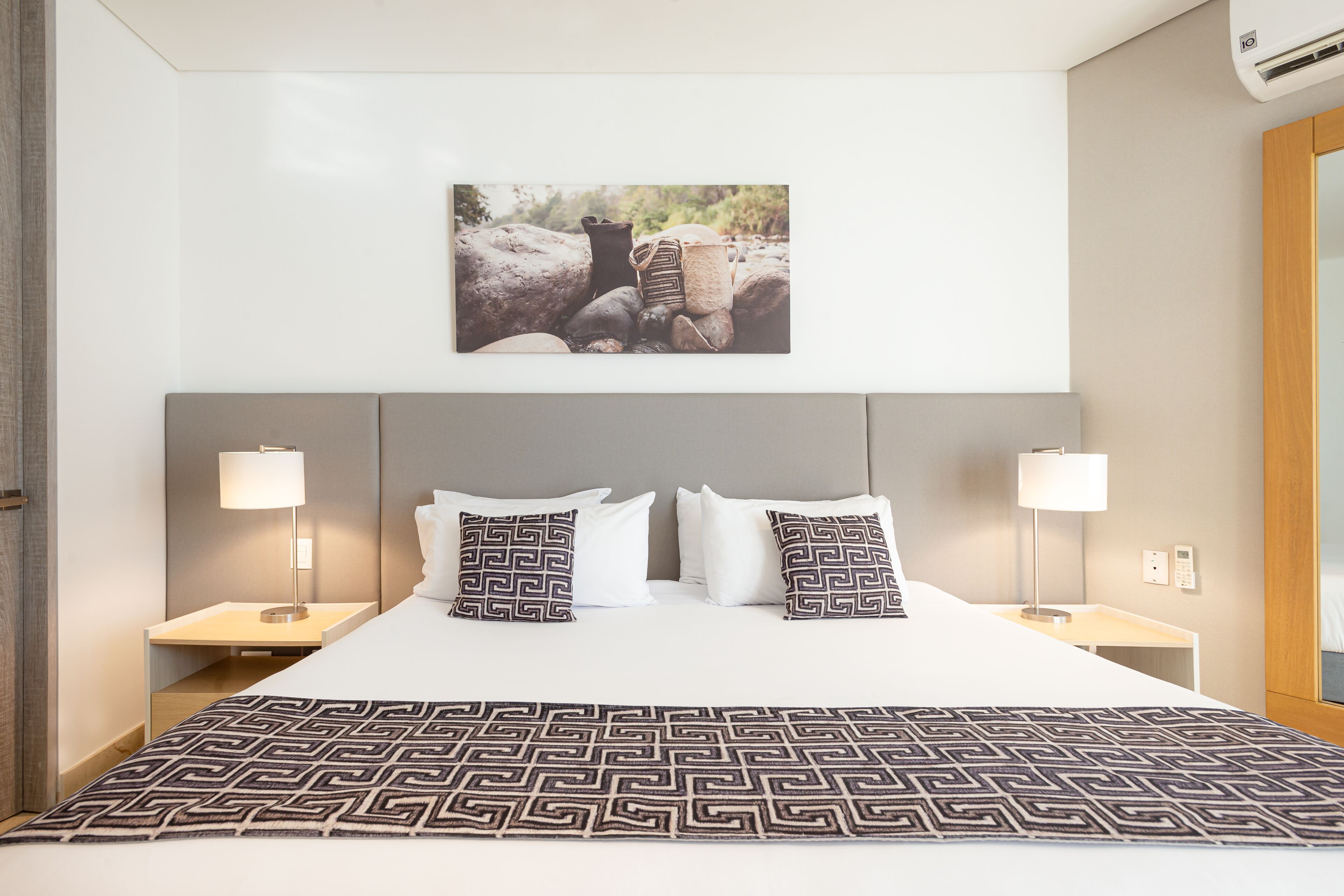 A hotel room with a large bed, two nightstands, a wall-mounted picture, and a wooden headboard.