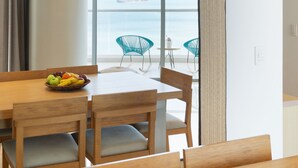 A dining area with a wooden table and chairs, a fruit bowl on the table, and a view of the sea through large windows. - Grand Marina Santa Marta (Santa Marta)