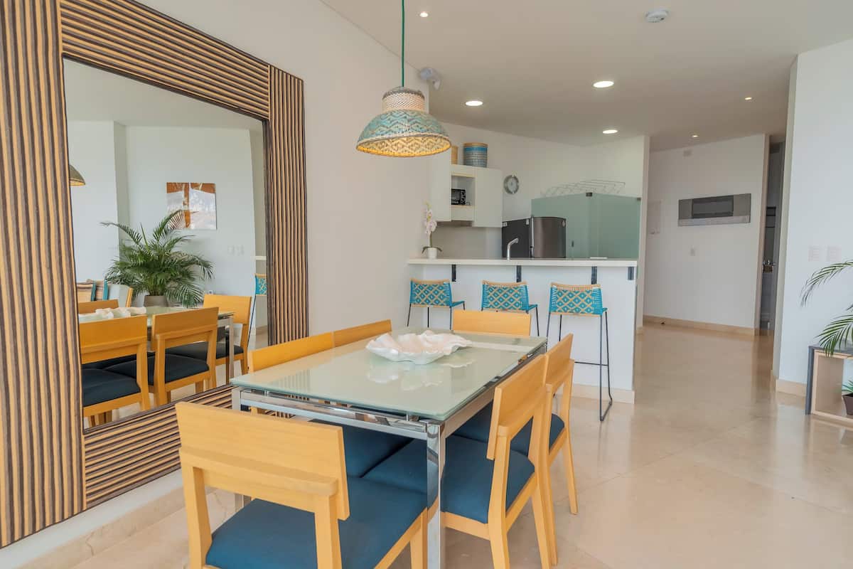 A modern dining area with a glass table, wooden chairs, and a hanging pendant light.