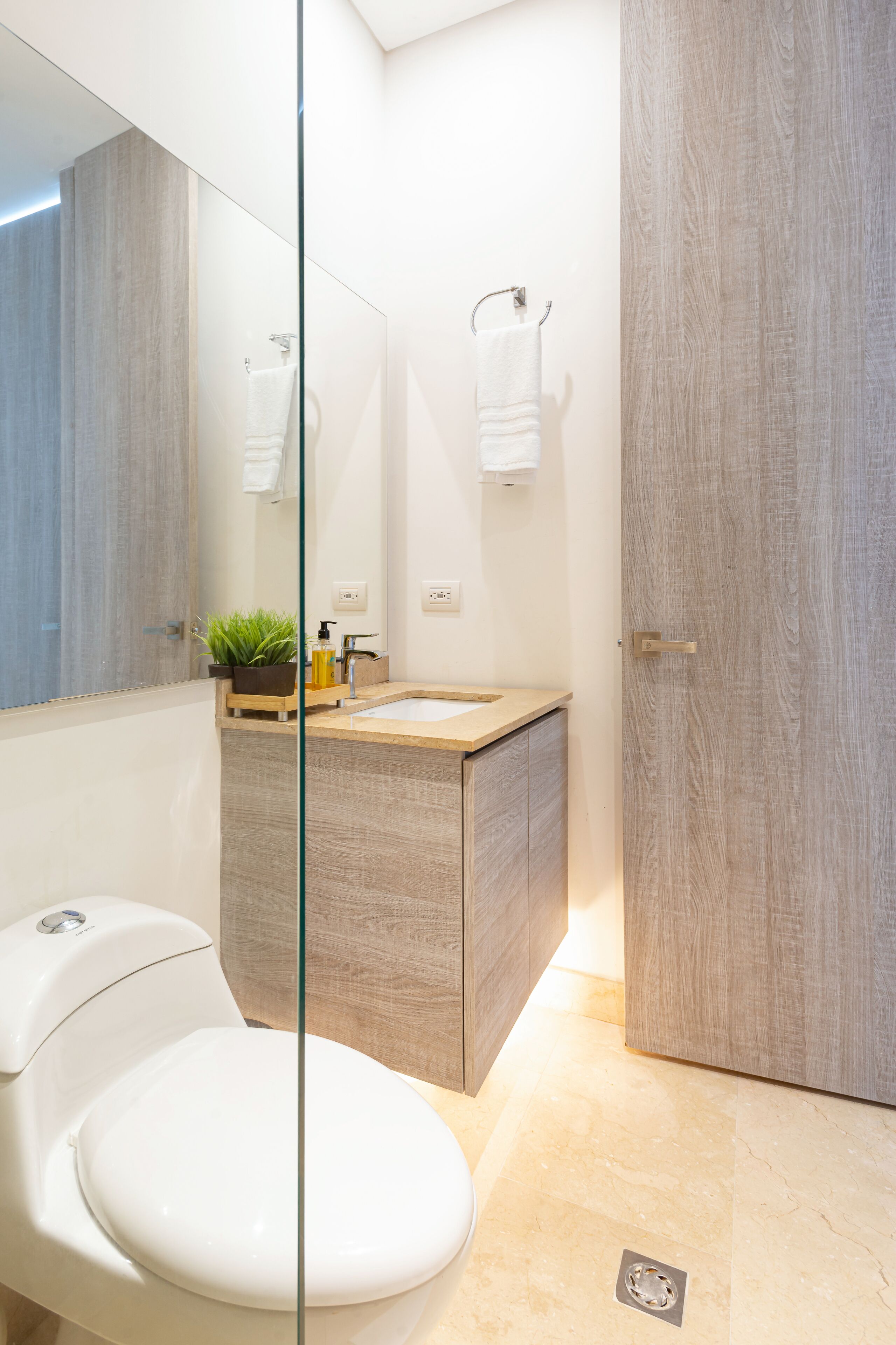 Une salle de bain moderne avec une paroi de séparation en verre, un meuble-lavabo en bois, des toilettes blanches et un porte-serviettes.