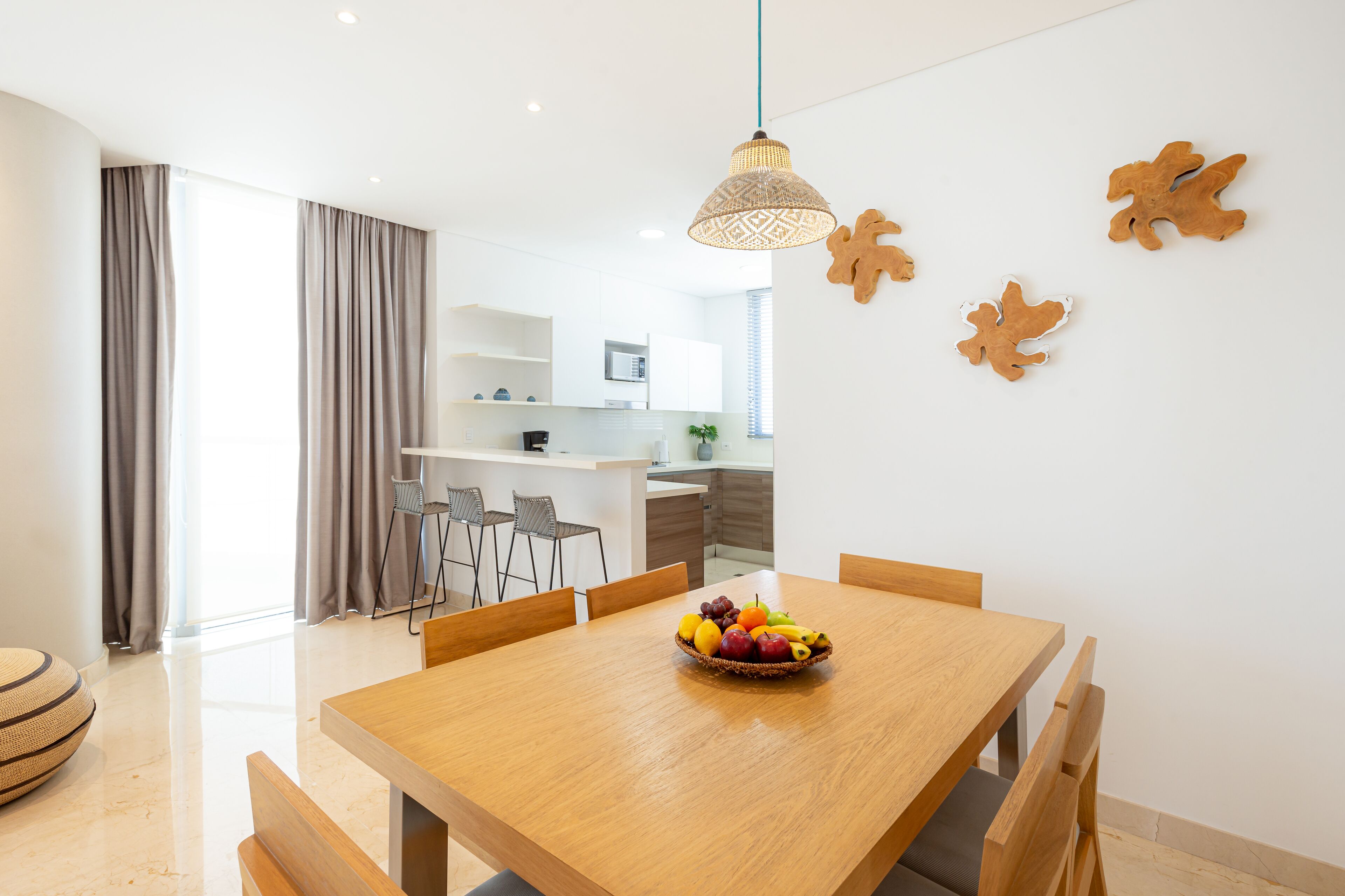 A modern dining area with a wooden table, chairs, and a fruit bowl.