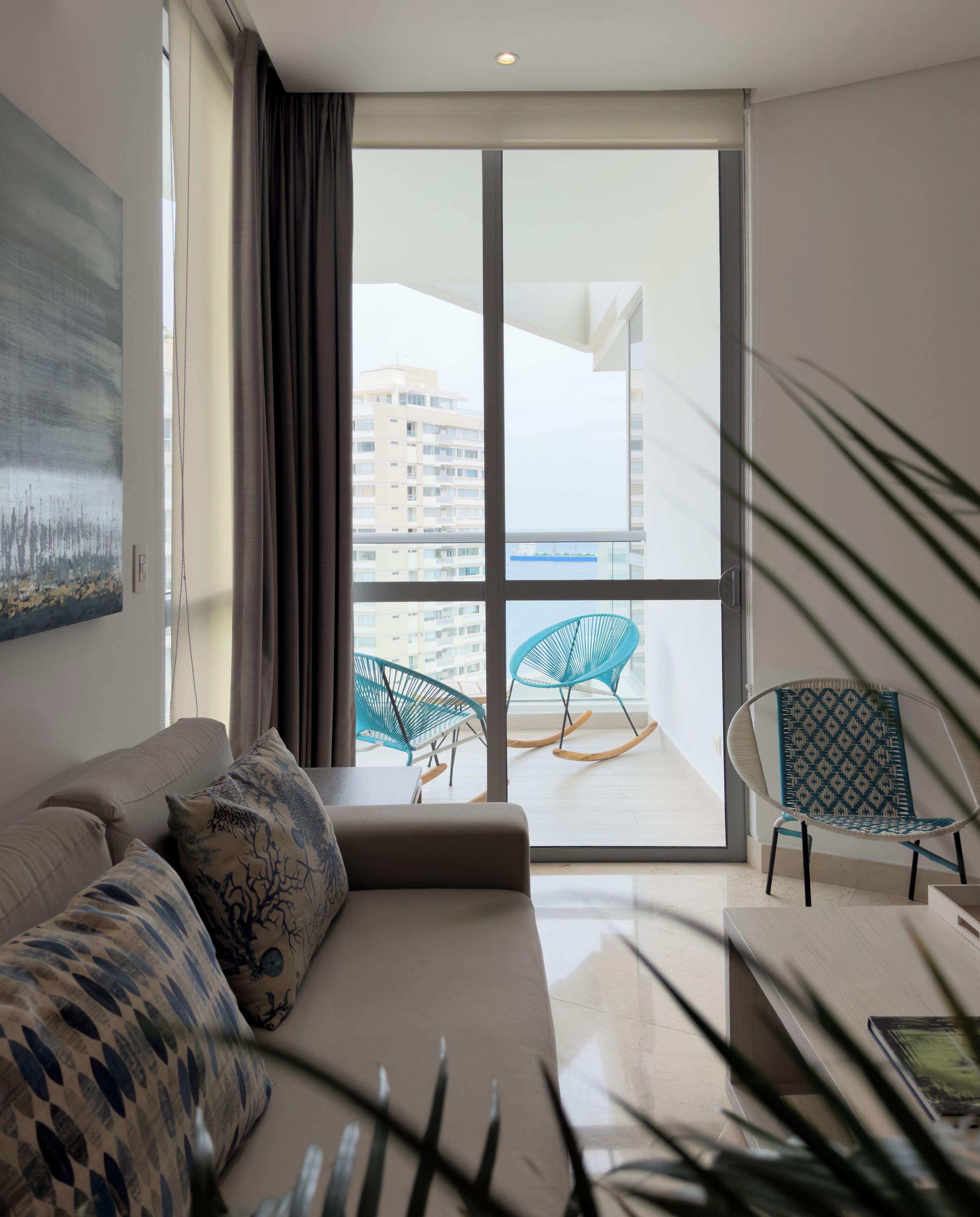 Una sala de estar moderna con un sofá, dos sillones, un ventanal y vista a un edificio.