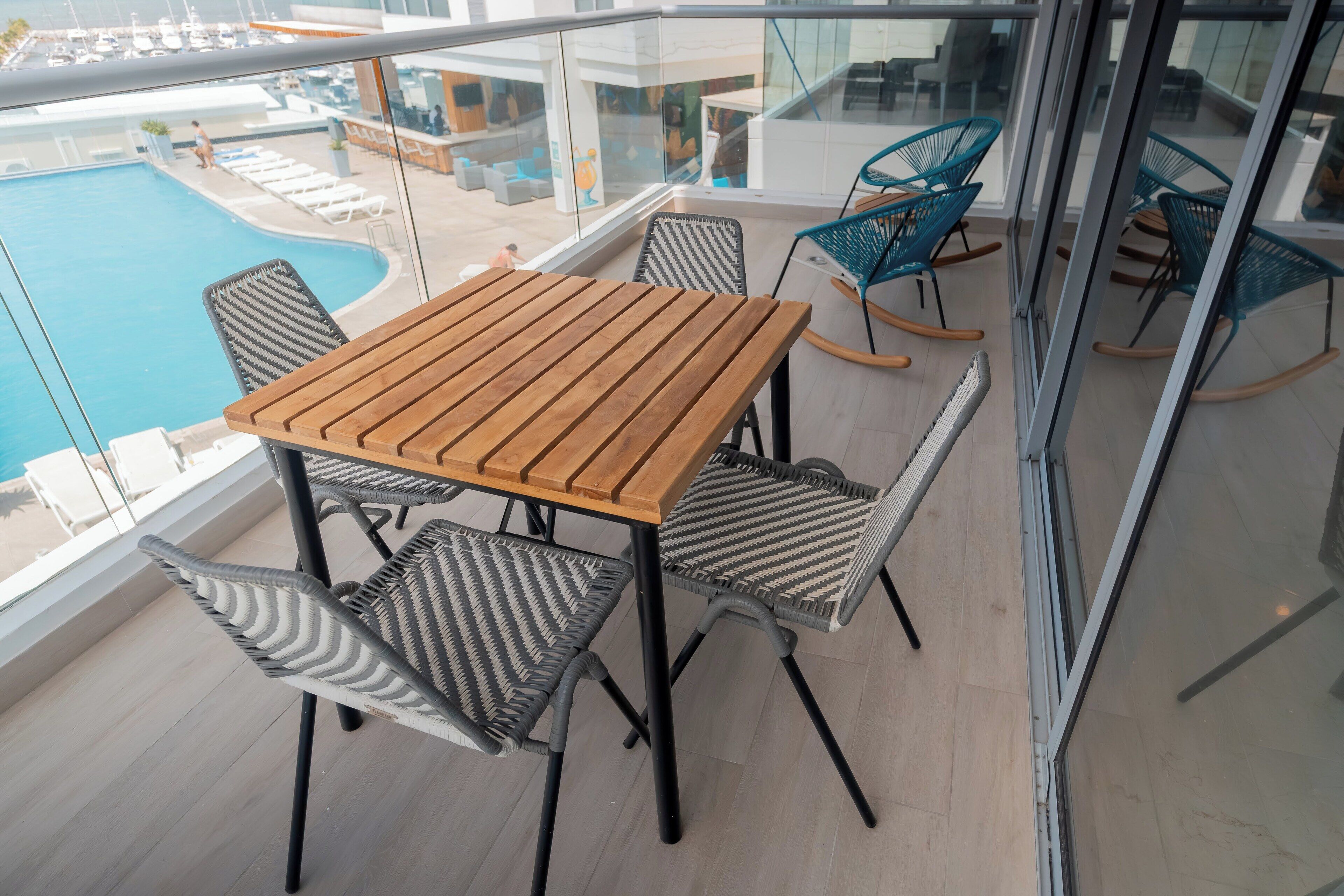 Een balkon met een houten tafel en rieten stoelen, met uitzicht op een zwembad en een loungegedeelte.