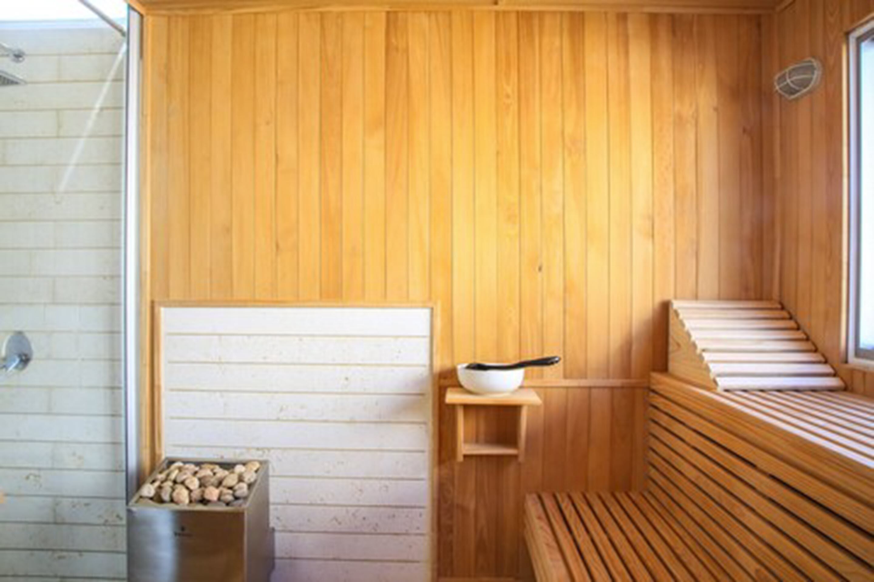 Un sauna en bois, avec des bancs et une petite étagère sur laquelle est posé un bol.
