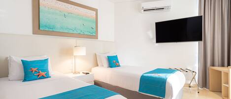 A hotel room with two beds, a TV, an air conditioning unit, and a painting of a beach scene.