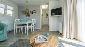 A modern living room with a dining area, a TV mounted on the wall, and a view into the kitchen. - Eureka Park (Renesse)