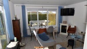 A modern living room with a rocking chair, a dining table, and a TV mounted on the wall. - Eureka Park (Renesse)