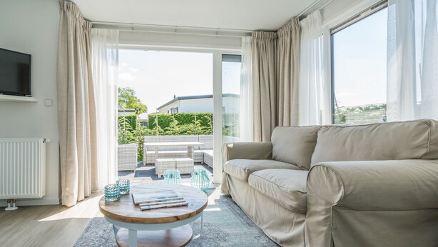 A modern living room with a beige sofa, a wooden coffee table, and a view of a balcony with outdoor furniture. - Eureka Park (Renesse)