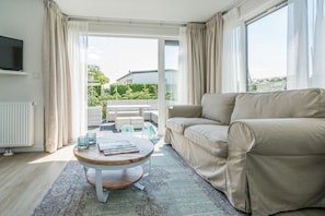 A modern living room with a beige sofa, a wooden coffee table, and a view of a balcony with outdoor furniture. - Eureka Park (Renesse)