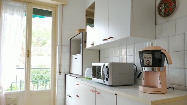 A kitchen with white cabinets, a microwave, a coffee maker, and a window with a view of greenery. - Holiday Apartment in Santa Margherita (Santa Margherita Ligure)