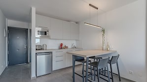 A modern kitchen with a built-in microwave, a coffee maker, and a sink. There are two bar stools and a hanging light fixture. - Costa Adeje Garden (Adeje)